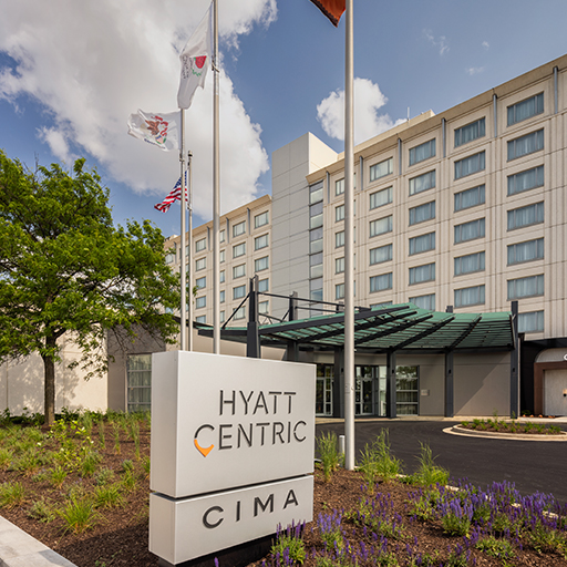 Exterior view of the Hyatt Centric hotel, with a large entrance canopy, flagpoles, landscaping, and a sign reading “Hyatt Centric Cima” in front.