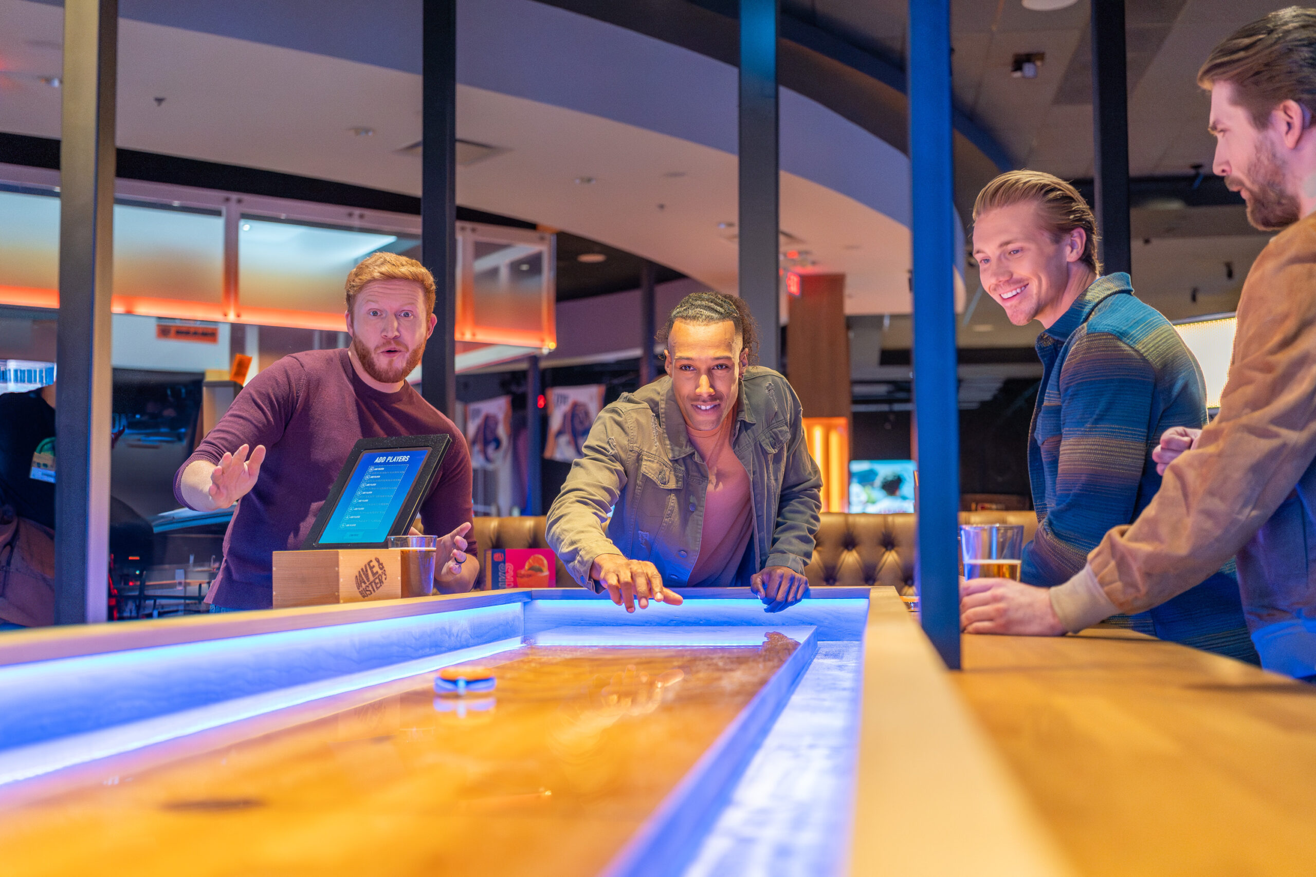 Three men playing a game of shuffleboard in an arcade.