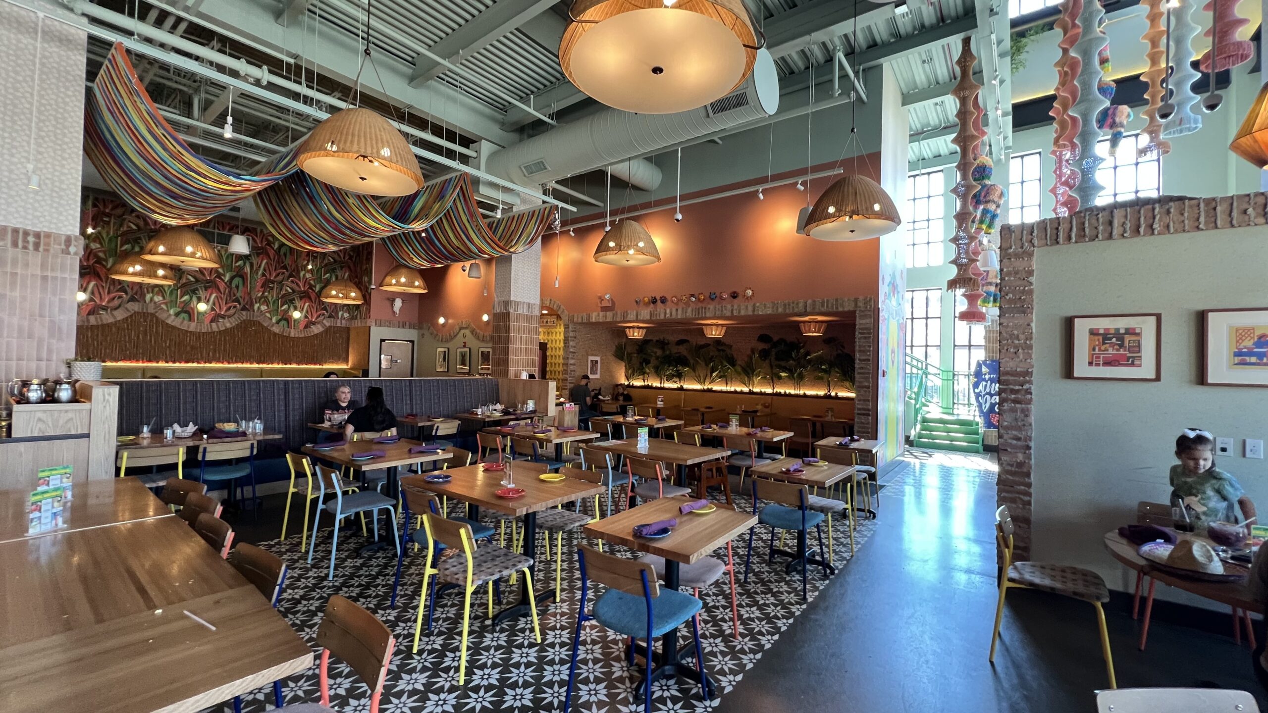 Interior of a colorful restaurant with wooden tables, mismatched chairs, and draped fabric ceiling decorations.