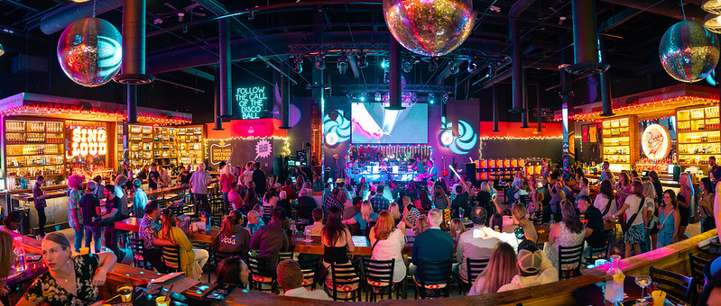 Crowded nightclub interior with a stage, dance floor, several disco balls hanging from the ceiling, and bars on either side.