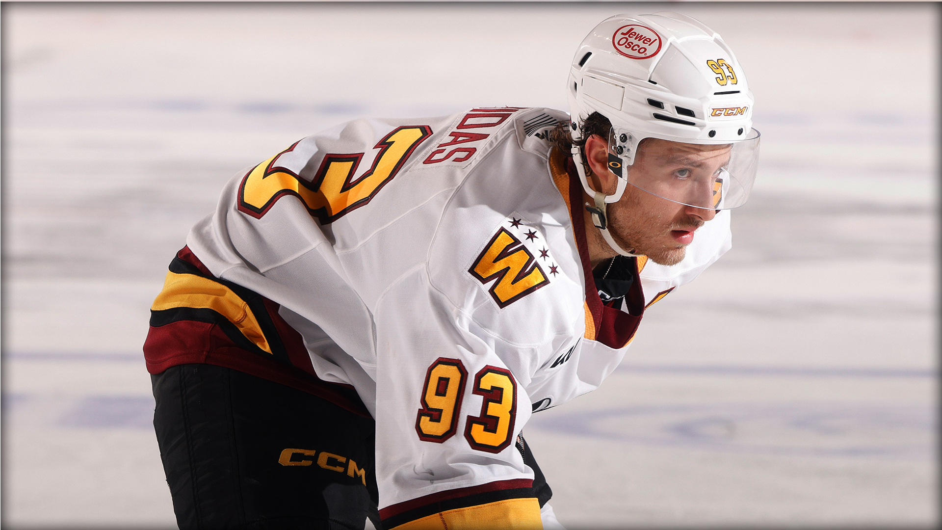 A hockey player in a white and yellow jersey with number 93 and a helmet is on the ice, looking forward and preparing for play.