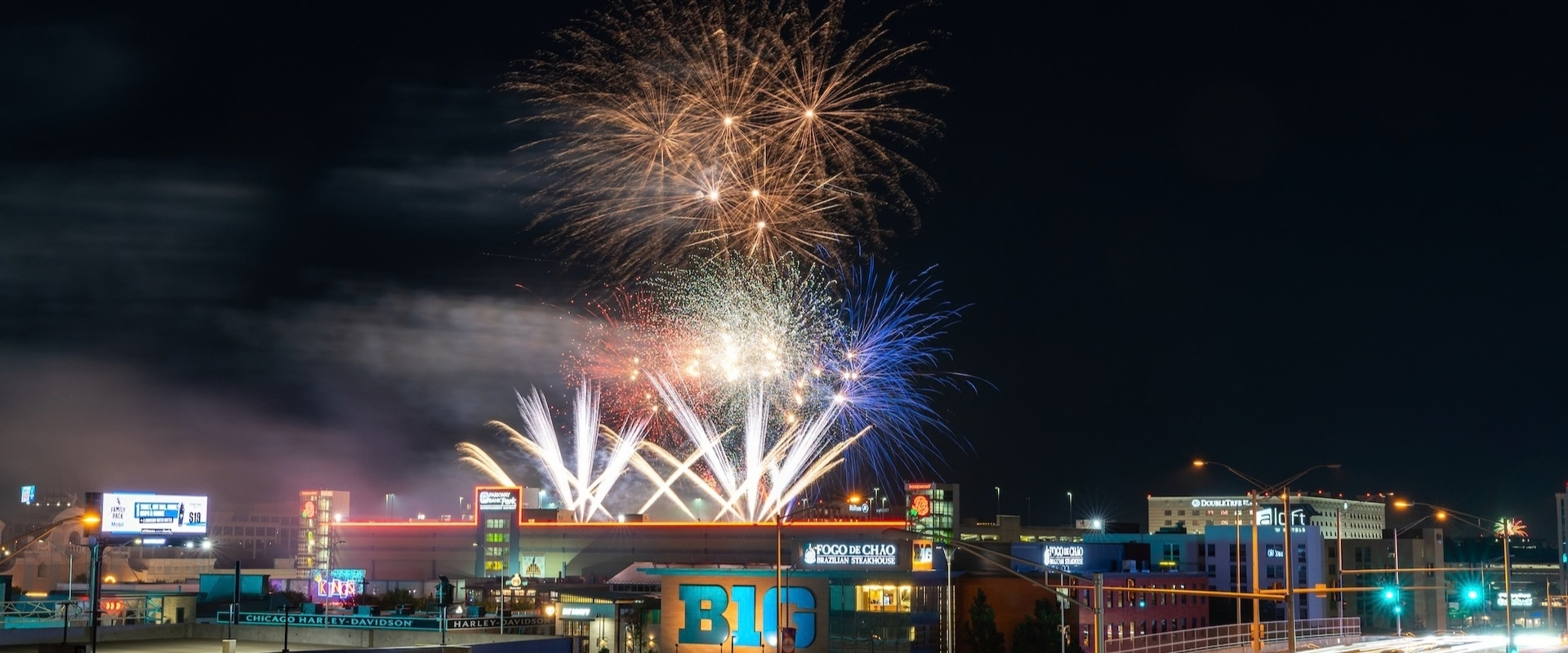 Fireworks exploding over a city skyline at night, with buildings visible in the foreground.
